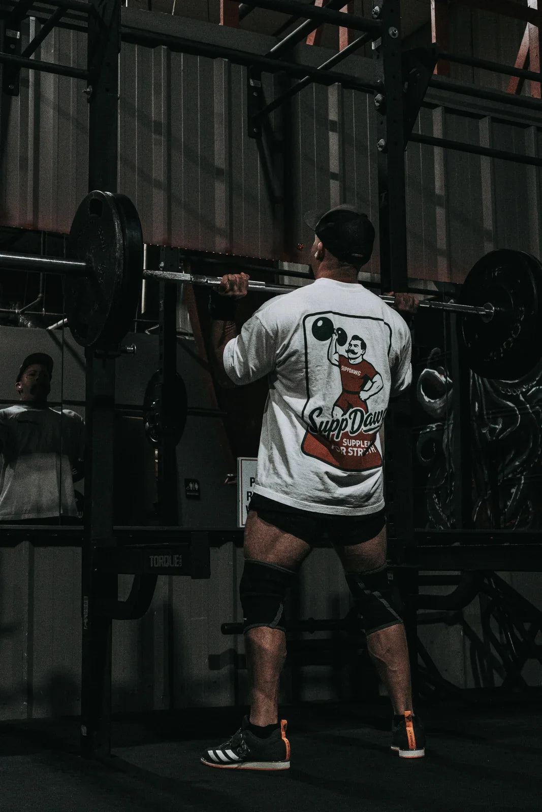 Athlete in a SuppDawg shirt preparing with a barbell in a squat rack
