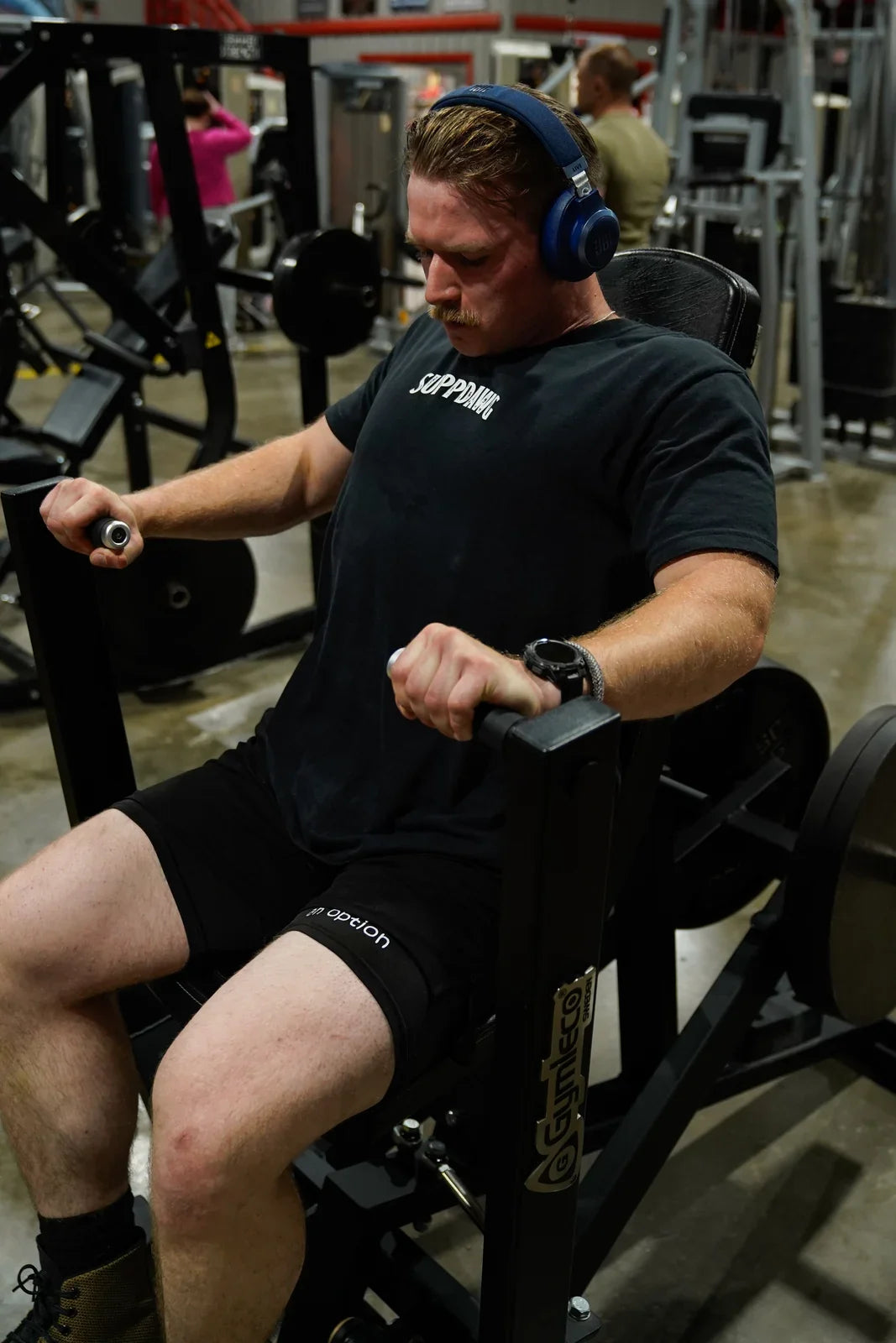 Athlete in a SuppDawg shirt seated at a resistance-training machine