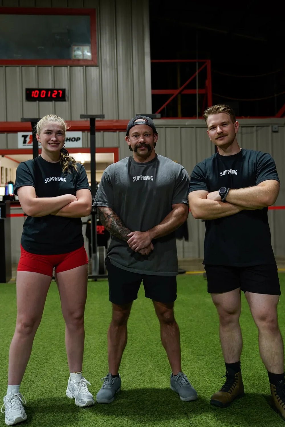 Three people in SuppDawg shirts standing together in a gym