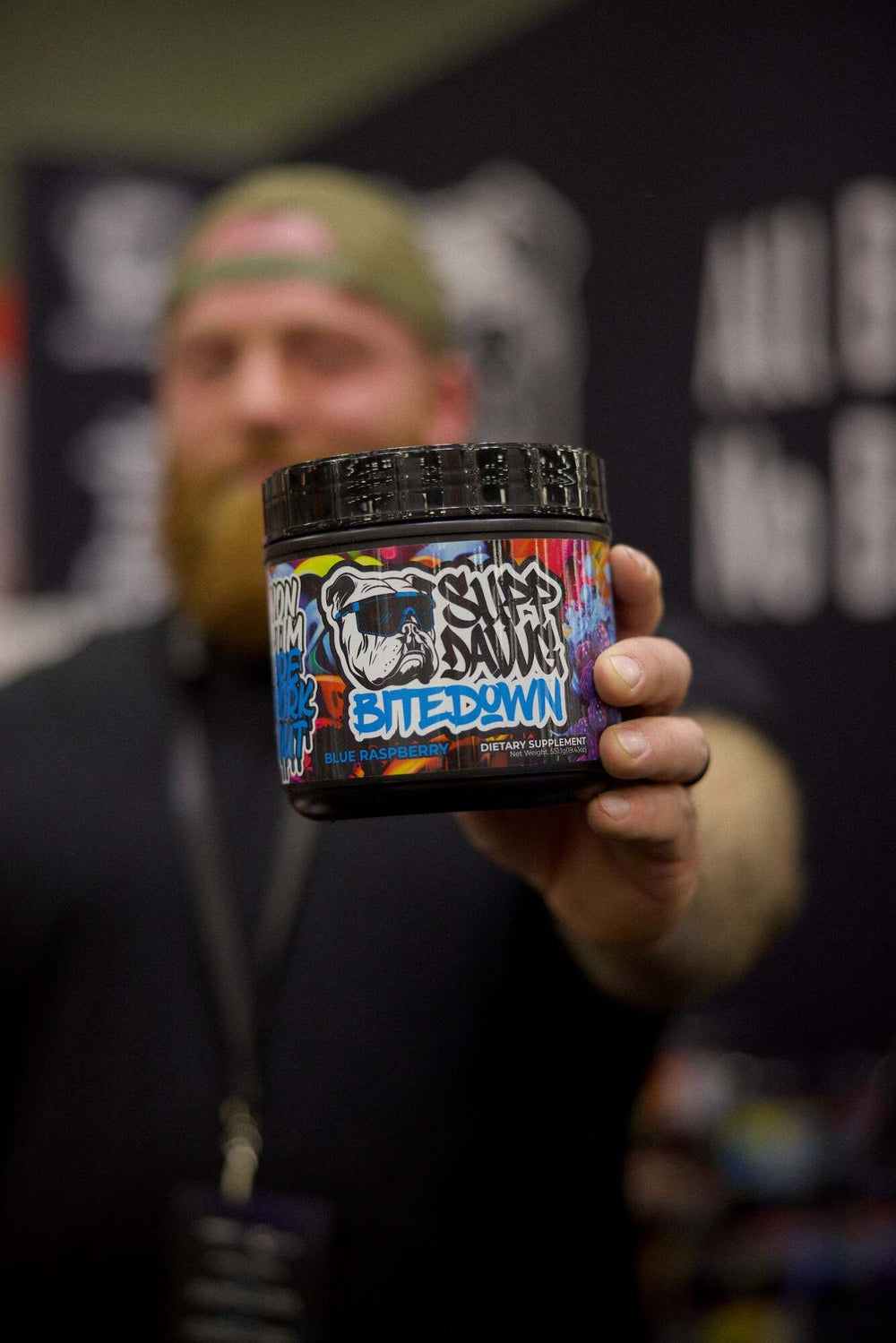 SuppDawg athlete holding a tub of Blue Raspberry Bite Down caffeine-free pre-workout
