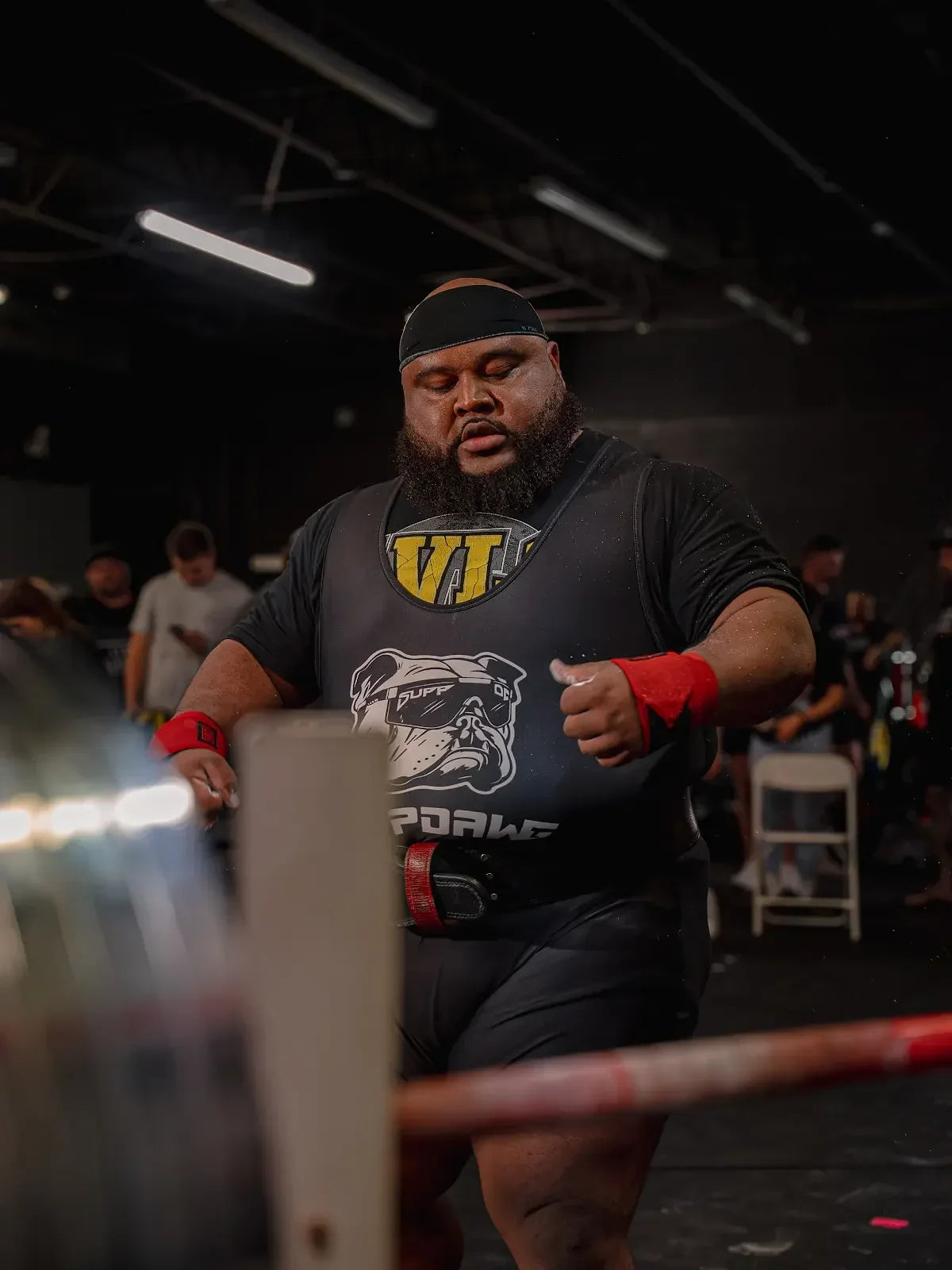 Strength athlete wearing a SuppDawg shirt and wrist wraps beside a barbell
