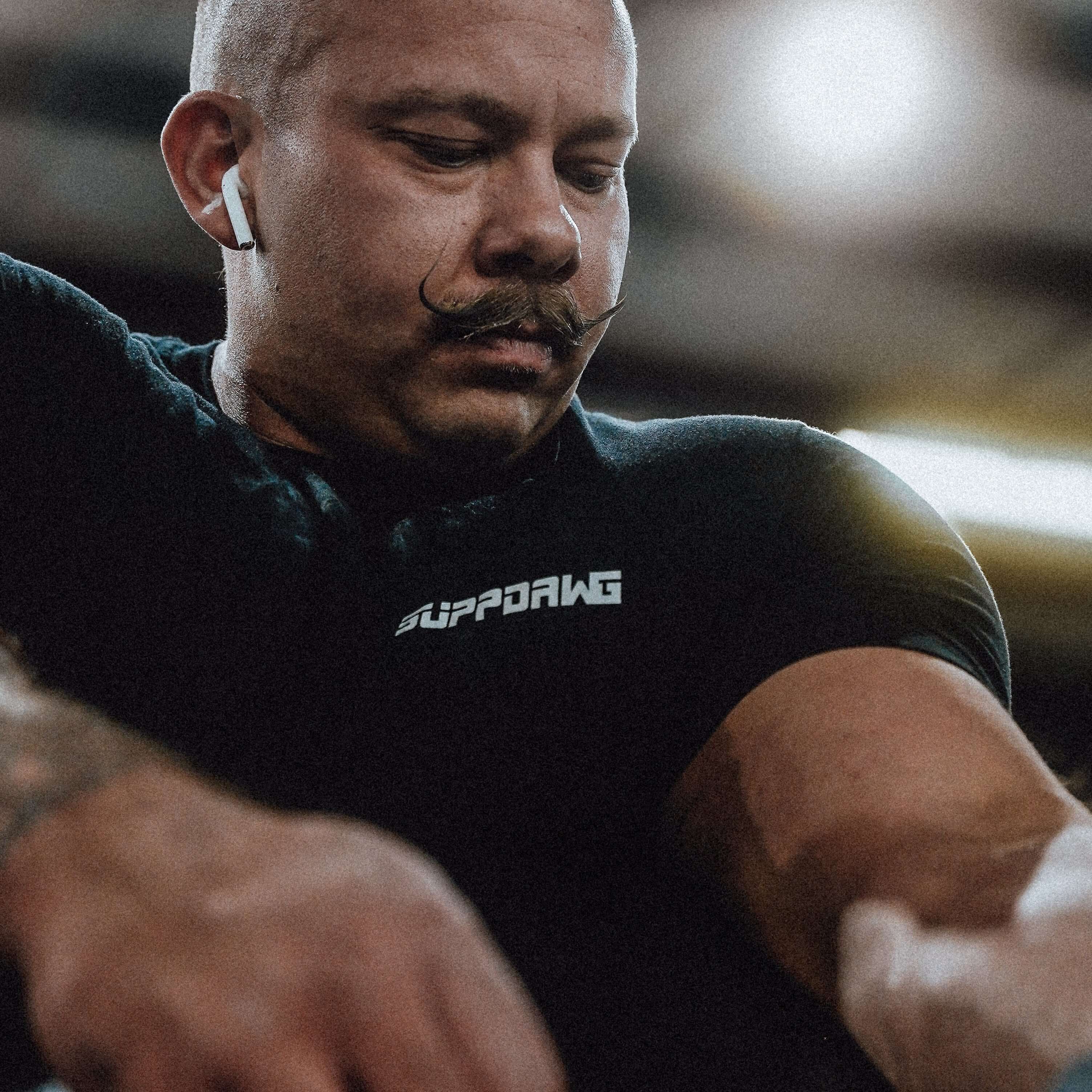 Man wearing SuppDawg logo performance fit t-shirt, showcasing comfort and style during a workout.